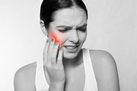 Lady holding her cheek grimacing with obvious mouth pain.