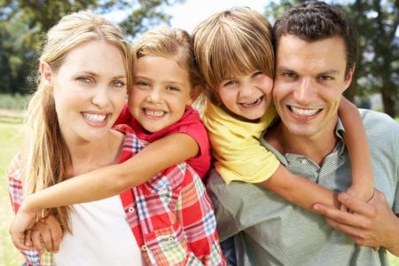 A woman, man, and two young children hugging and smiling at the camera